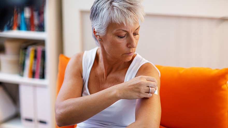 A woman in menopause sticks a transdermal patch on her arm.